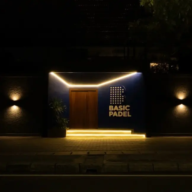 Lit wooden doorway with the Basic Padel logo at night
