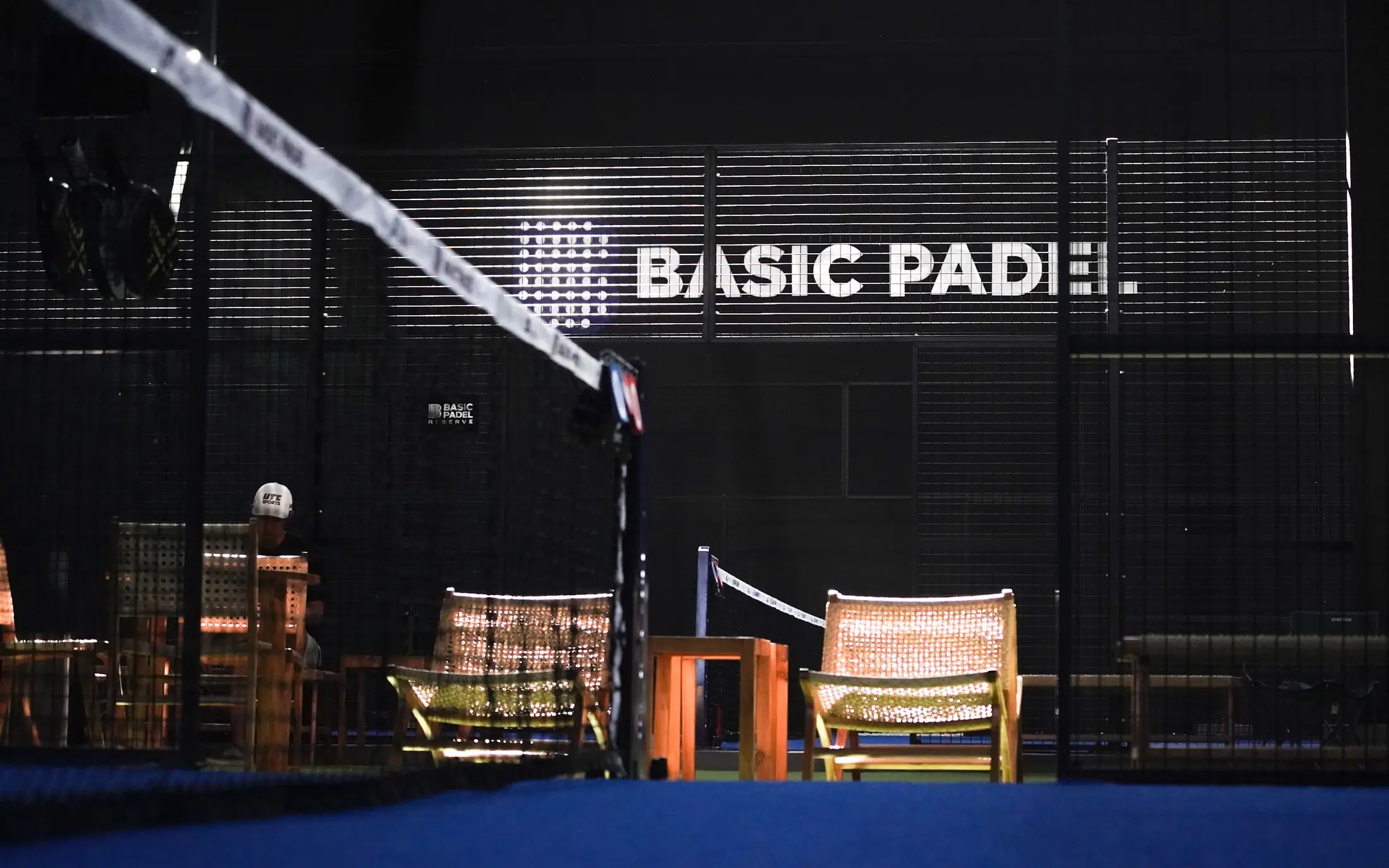 Rattan chairs on green turf behind the net, under the Basic Padel sign